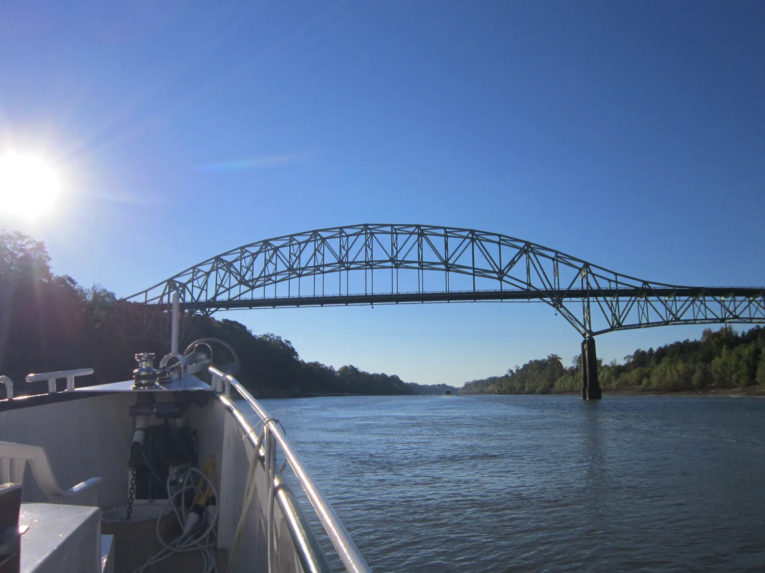 A sunlit steel arch bridge and distant tow framed beyond Sage's bow rail
